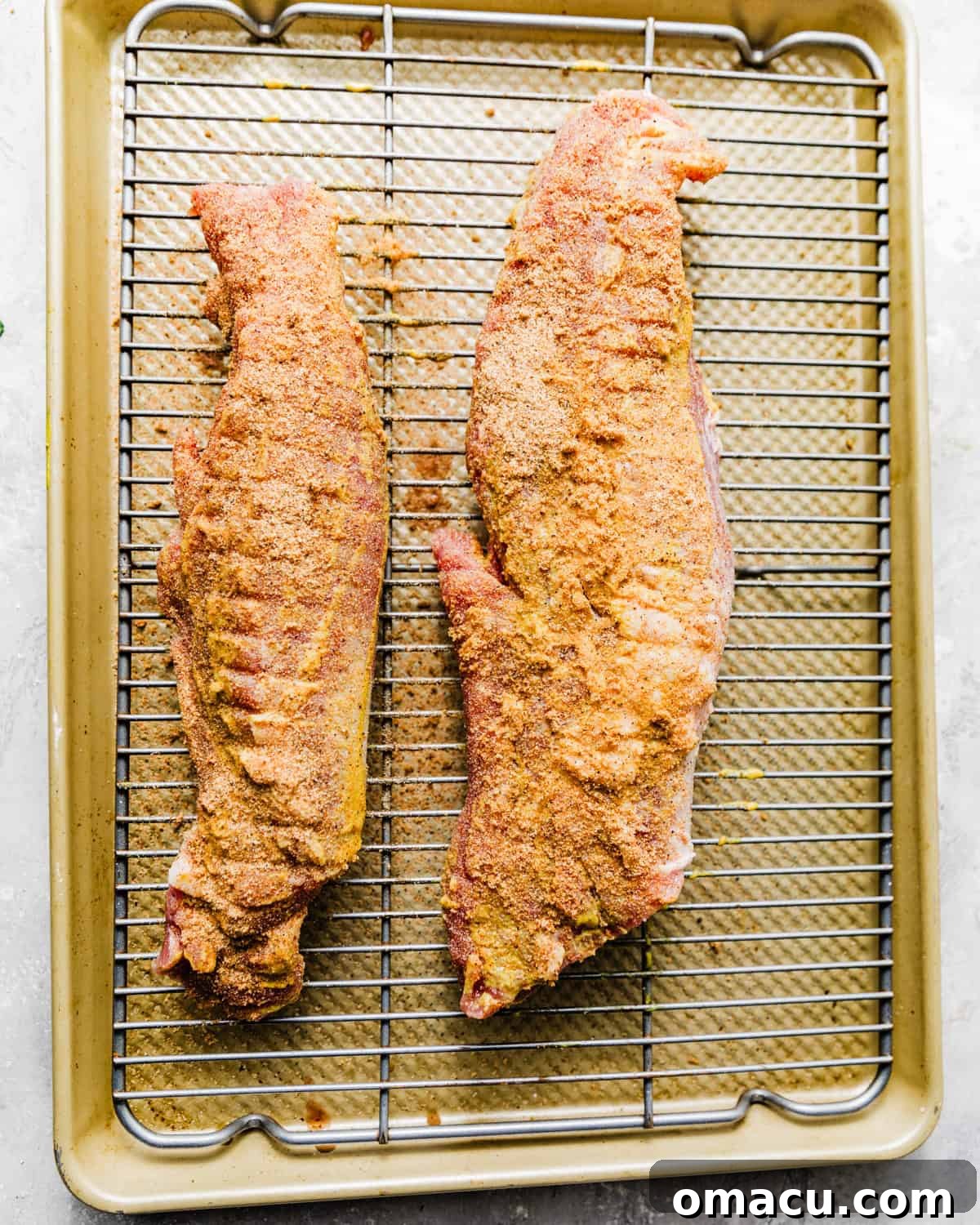 Pork tenderloin generously coated in the honey mustard base and spice rub, positioned on a wire rack over a baking sheet.