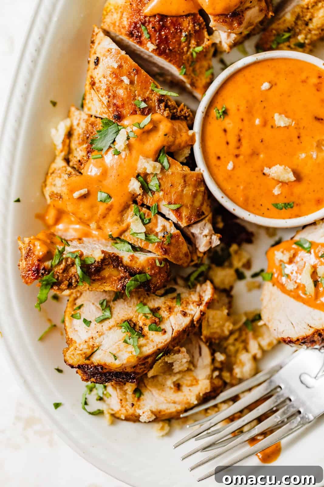Platter of perfectly sliced oven baked pork tenderloin medallions, served with a small bowl of rich Cajun cream sauce on the side, ready to be enjoyed.