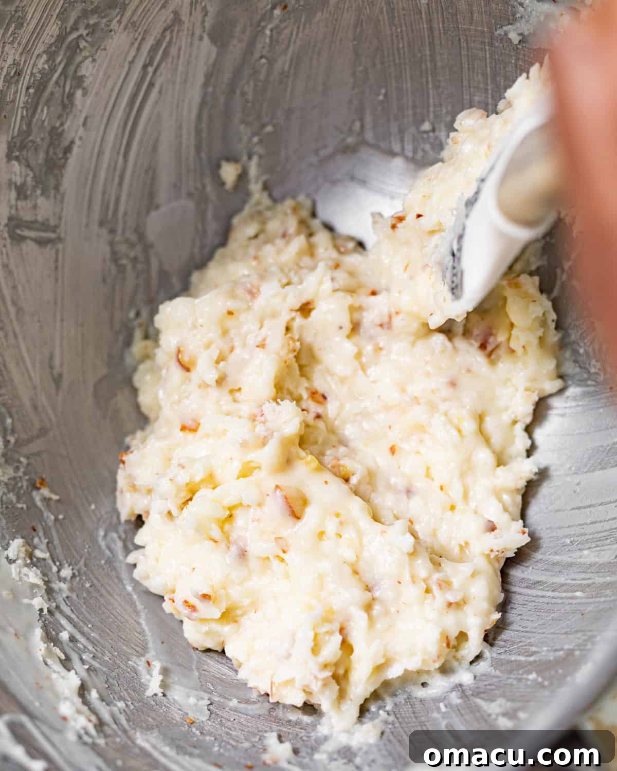 A rich and creamy coconut crunch glaze in a mixing bowl, featuring visible almond pieces and shredded coconut, ready to top the cooled pound cake.