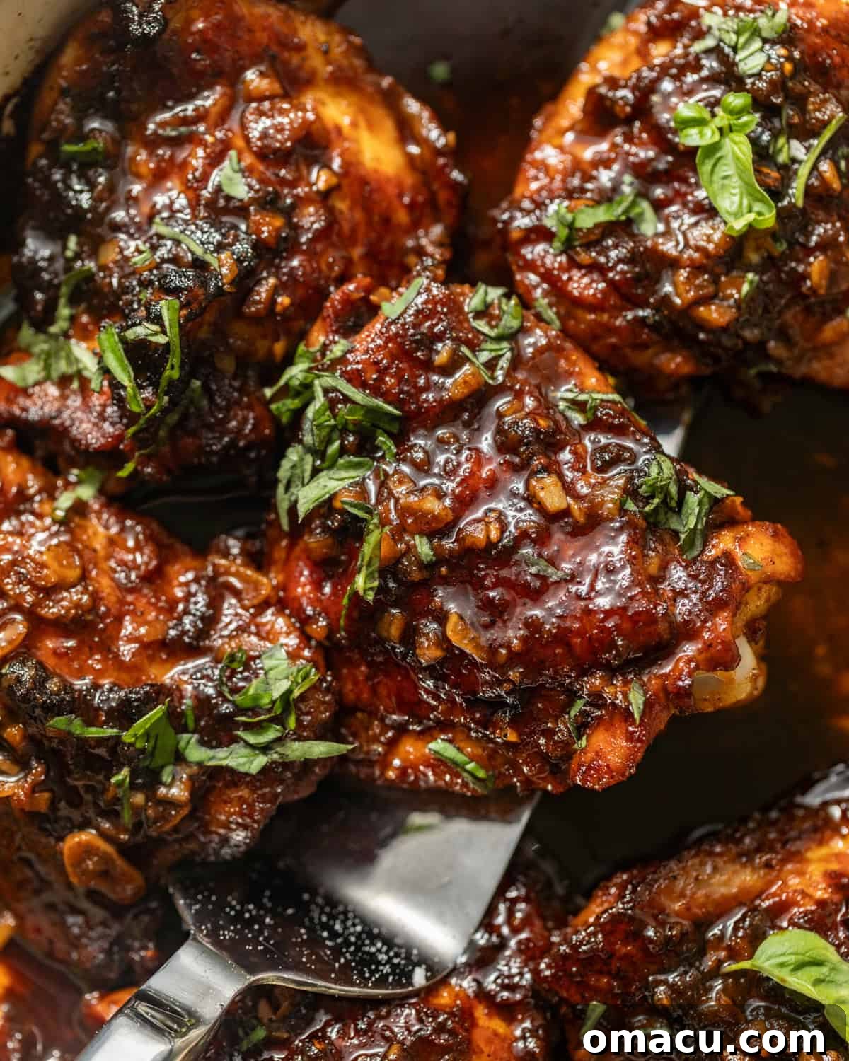 A serving spoon scooping sticky, glazed honey garlic chicken thighs from a pan, showing off the rich sauce.