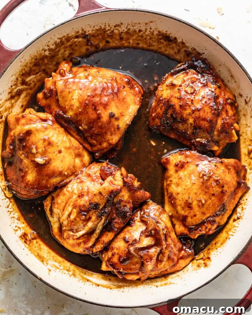 Seared chicken thighs coated in the sticky honey garlic sauce, nestled in a skillet and ready for baking.