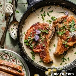 pan seared pork chops in a skillet with a garlic butter sauce on top.