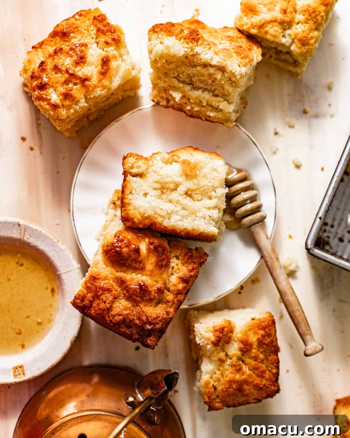 Platter of golden-brown butter swim biscuits with a honey dipper, showcasing their crispy edges and inviting texture.