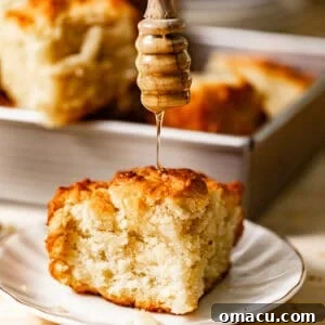 A butter swim biscuit on a plate with honey being drizzled on top, showcasing its golden crust and fluffy interior.