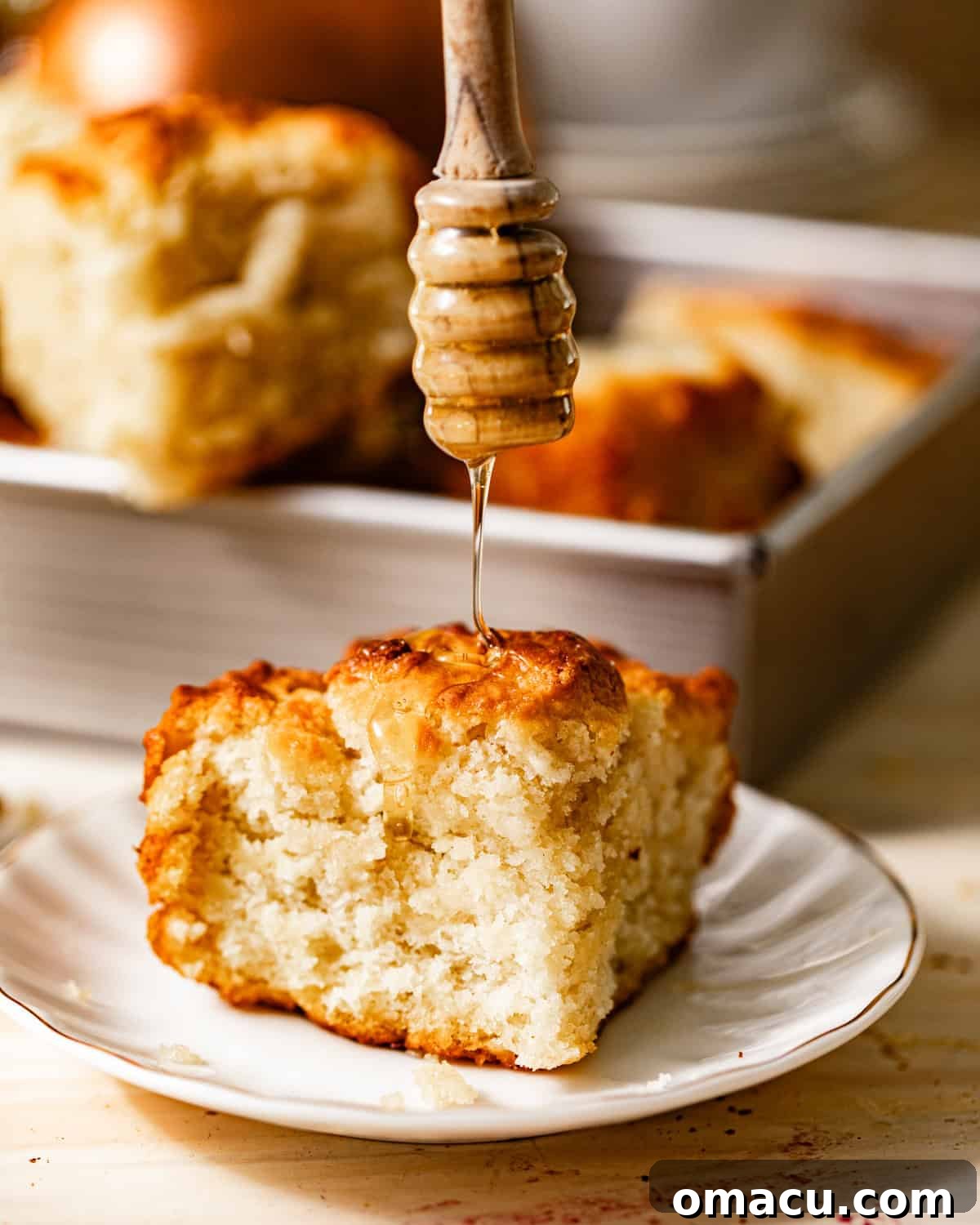 A single butter swim biscuit on a plate, with golden honey being generously drizzled over its fluffy top, highlighting its perfect texture.
