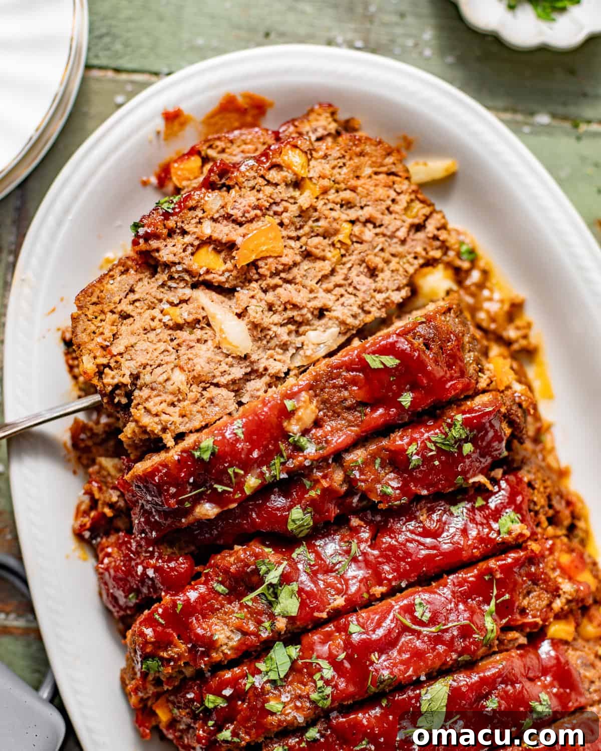 sliced bbq meatloaf on a serving plate garnished with fresh parsley.