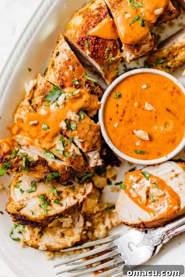 sliced baked pork tenderloin on a plate with cajun sauce and fresh parsley on top.