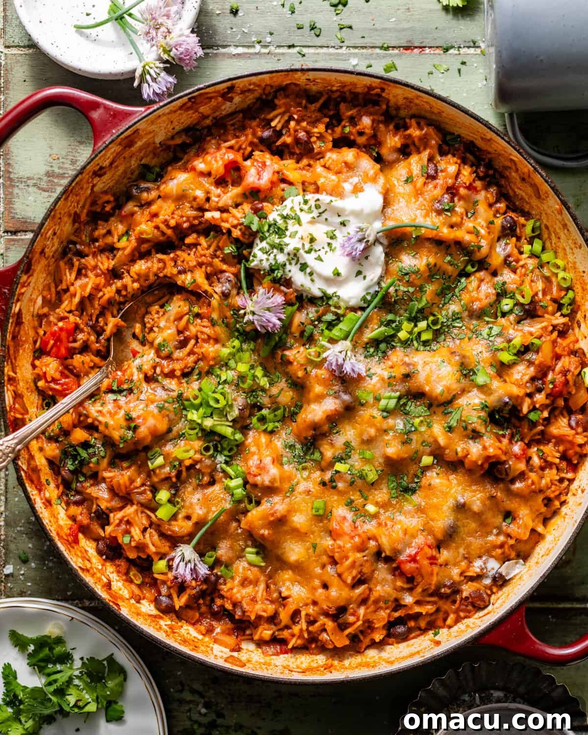 taco rice in a large skillet topped with sour cream, cheese, and diced chives and green onions.