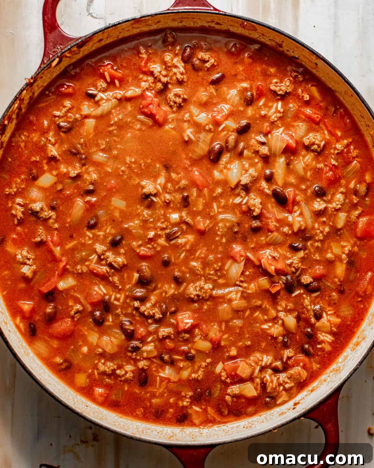 cooked ground beef with rice and veggies in a large skillet with tomatoes, beef broth, and black beans.