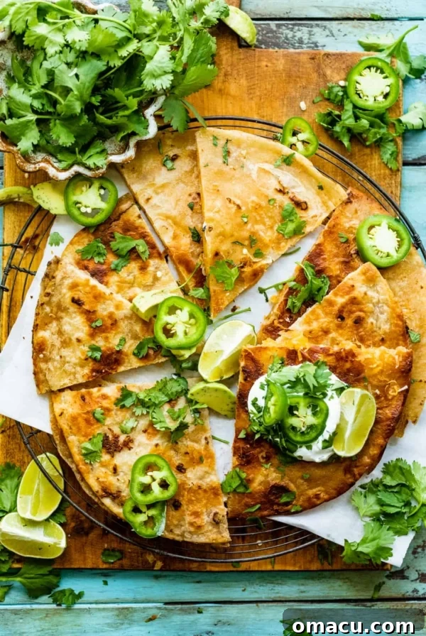 cheese quesadilla on a serving board garnished with limes, jalapenos, and cilantro.