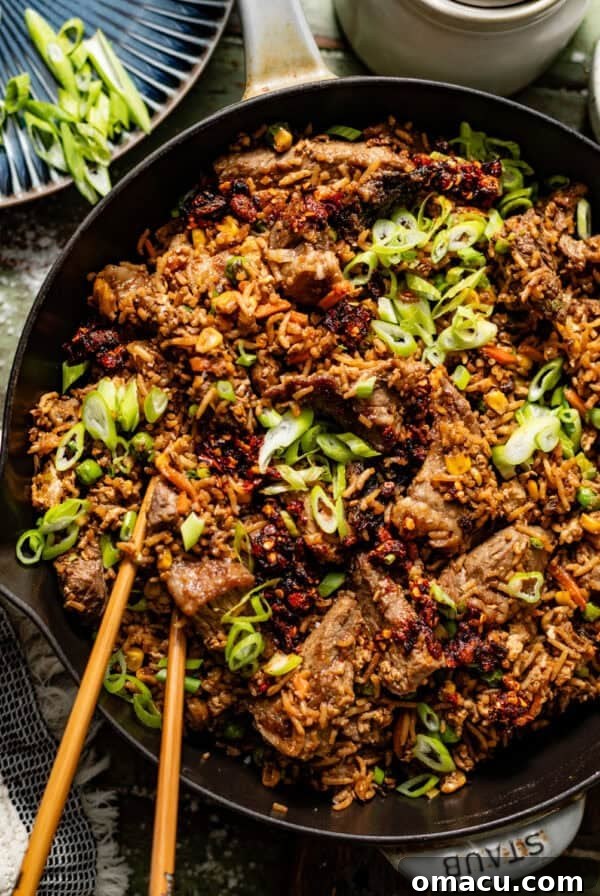 steak fried rice in a skillet topped with diced green onion and chopsticks.