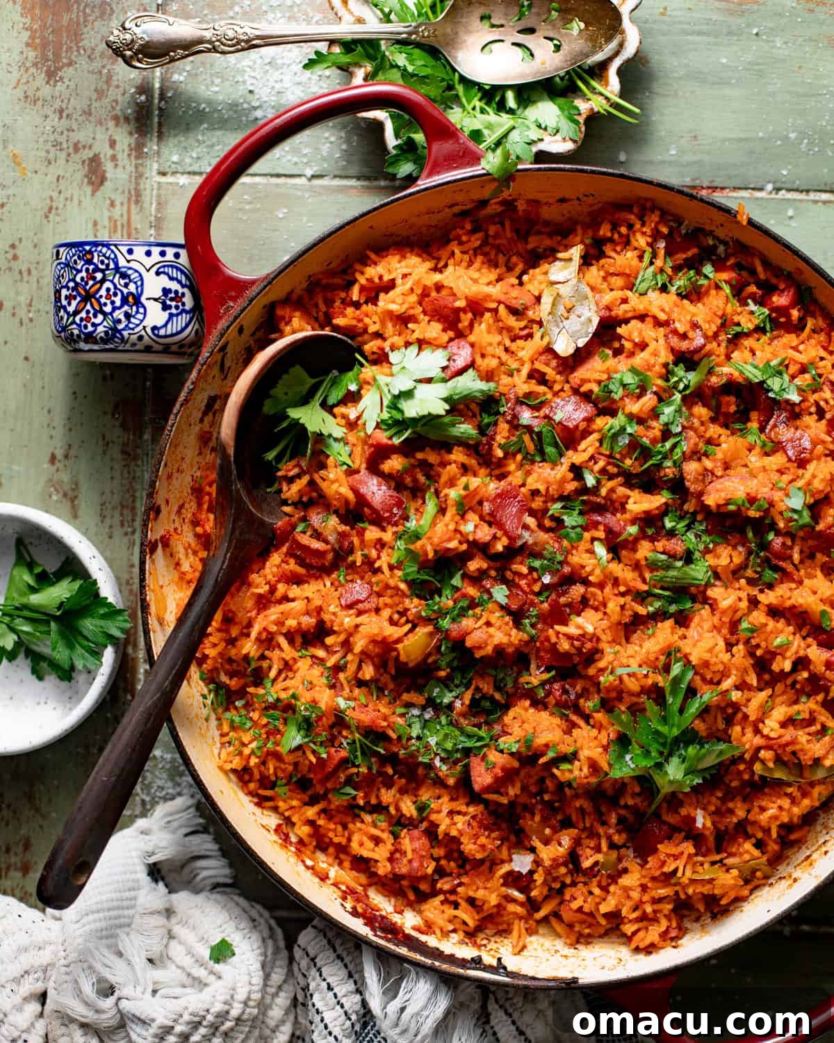 gullah red rice in a pot topped with fresh parsley with a wooden spoon scooping the rice.