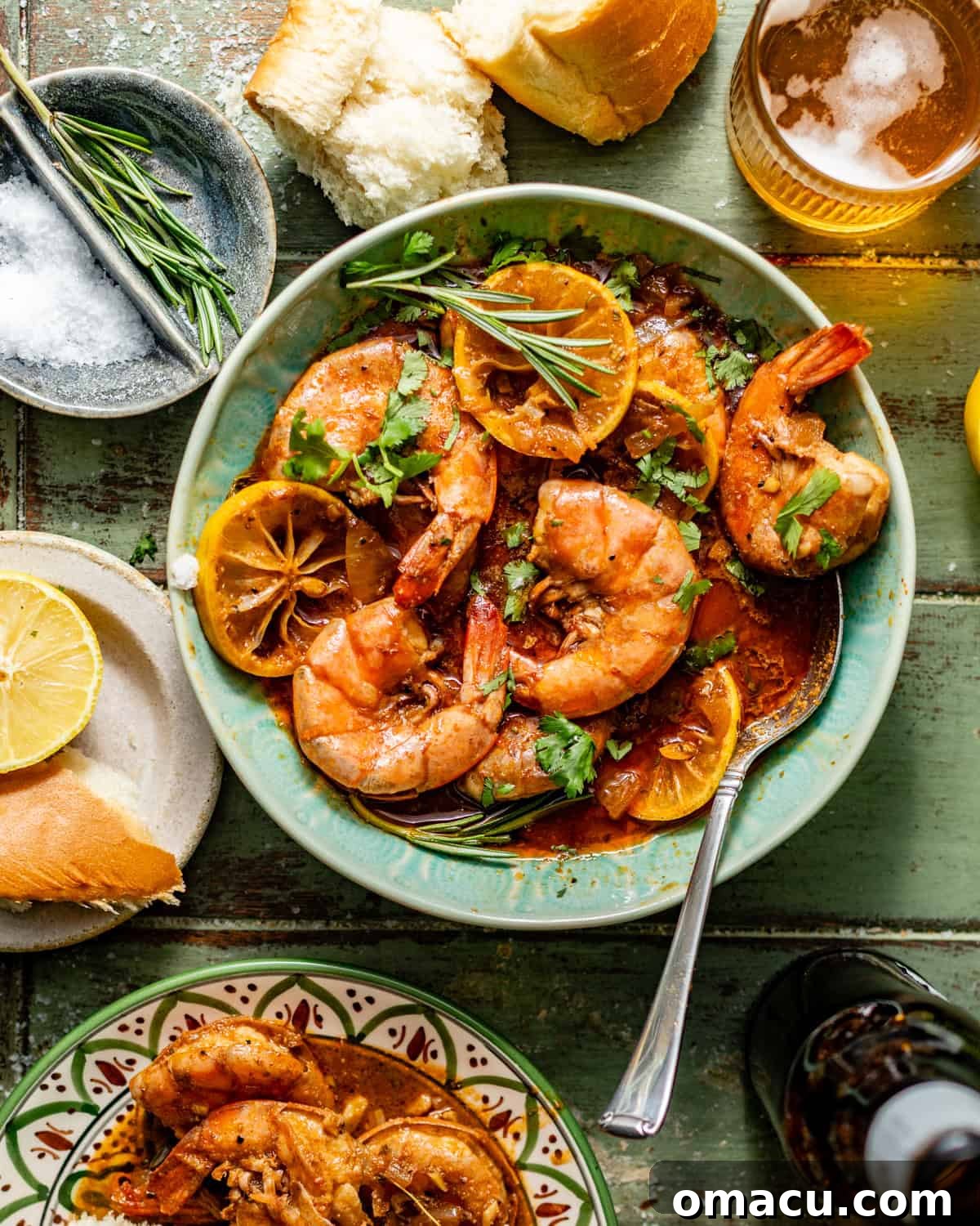 new orleans bbq shrimp in a bowl with sliced lemon next to a glass of sweet tea.