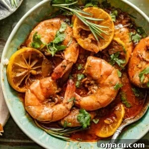 new orleans bbq shrimp in a bowl with a spoon garnished with fresh parsley and rosemary alongside a piece of crusty bread.