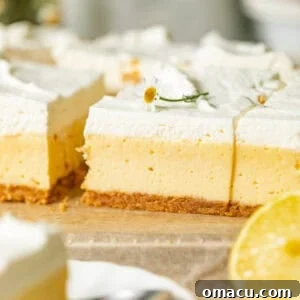 creamy lemon bars with graham cracker crust on a piece of parchment paper topped with edible flower and lemon whipped cream.