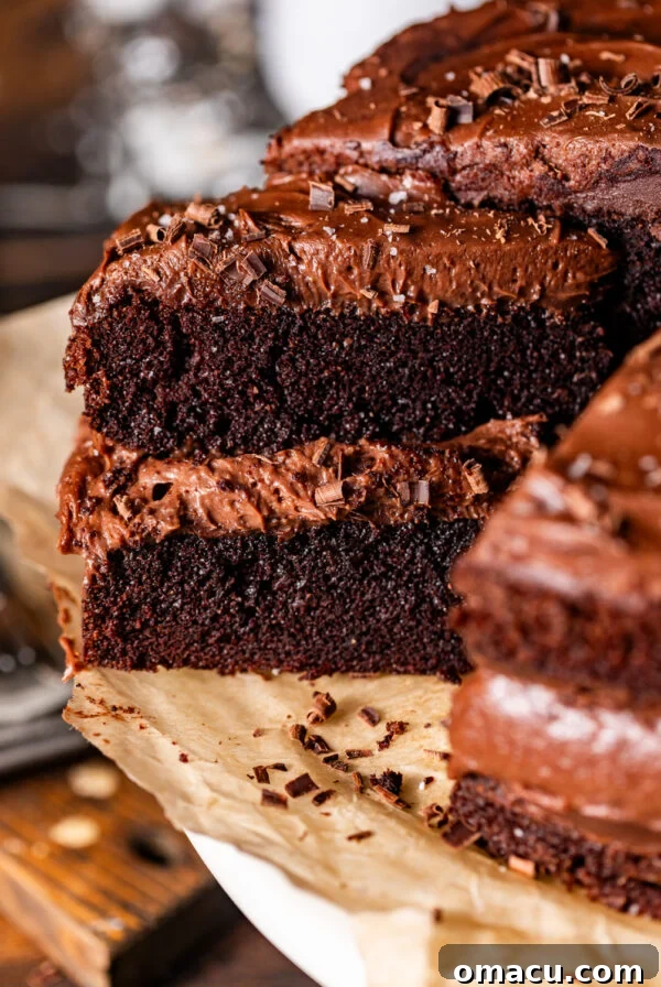 a slice of chocolate cake with chocolate mousse on a cake stand lined with parchment paper.
