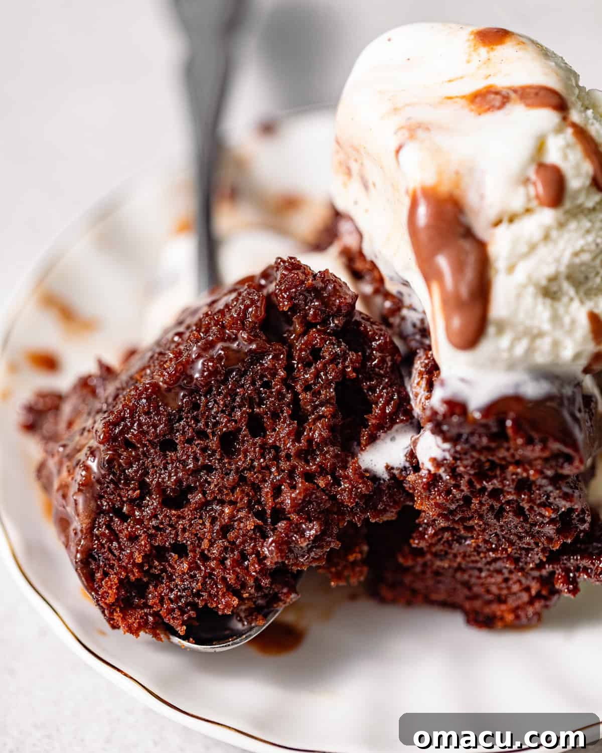 a bite size piece of chocolate sticky toffee pudding on a spoon with ice cream. 