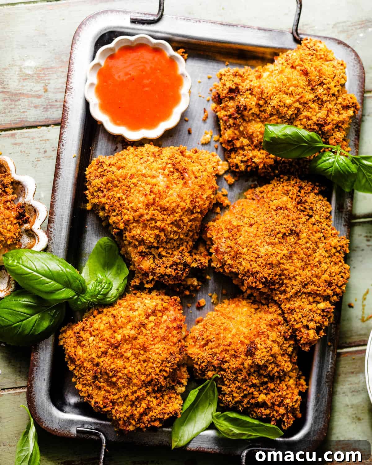 Crispy Oven-Baked Chicken That Tastes Like Fried Chicken 3 oven baked fried chicken on a serving tray garnished with fresh herbs and hot sauce.