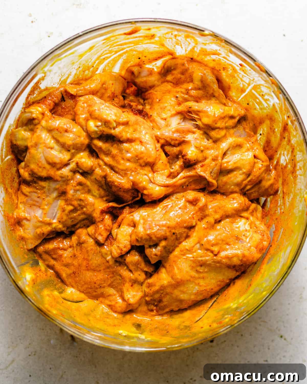 Crispy Oven-Baked Chicken That Tastes Like Fried Chicken 4 chicken thighs in a mixing bowl coated in seasonings and chicken marinade.