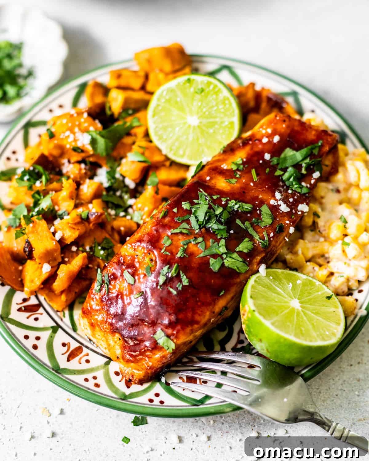 bbq salmon on a plate with sweet potatoes and corn and garnish with a lime and fresh parsley.