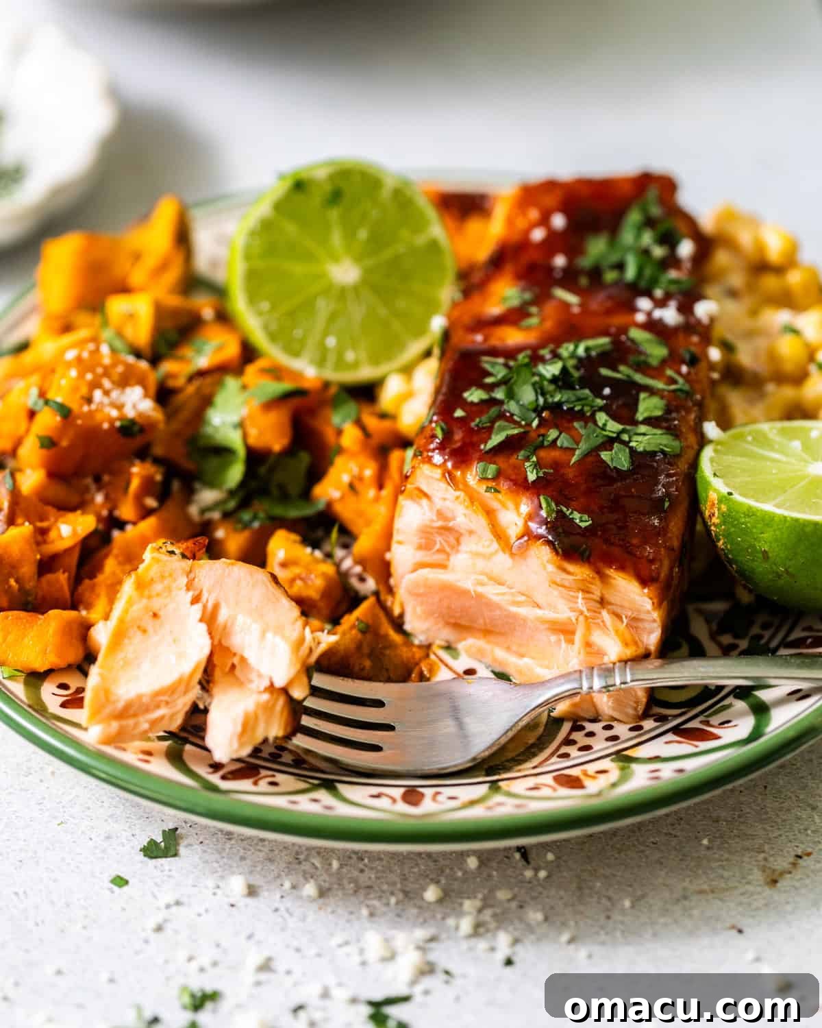 baked bbq salmon on a plate with a fork taking a piece off of the salmon to show the tender flaky texture. 