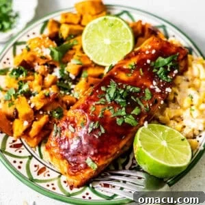 bbq salmon on a plate with sweet potatoes and corn and garnish with a lime and fresh parsley.