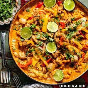 chicken fajita pasta in a large skillet topped with cilantro and sliced limes.