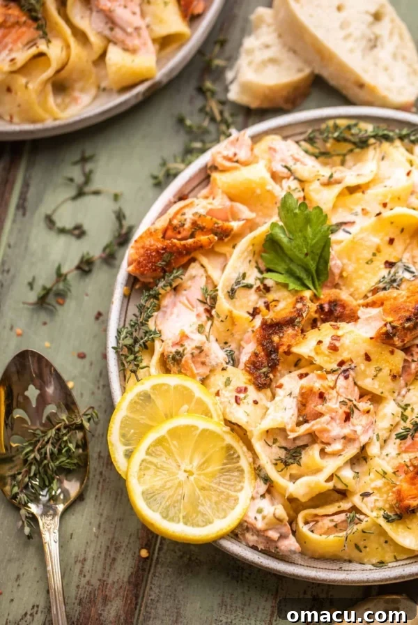 salmon pasta on a plate with lemon and a spoon next to the plate with fresh thyme