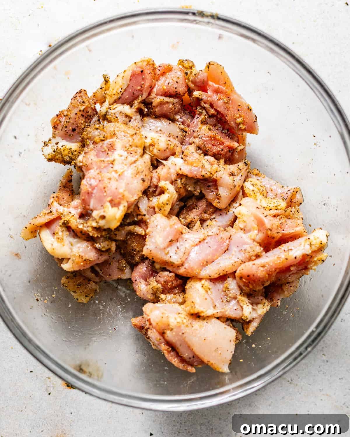 Garlic Butter Chicken Bites Recipe — Quick Savory Weeknight Meal 4 chicken thighs cut into bite sized chunks and coated in seasonings in a bowl.