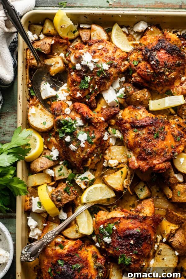 Garlic Butter Chicken Bites Recipe — Quick Savory Weeknight Meal 10 sheet pan chicken thighs and potatoes on a baking sheet with serving forks and garnished with feta and fresh parsley.