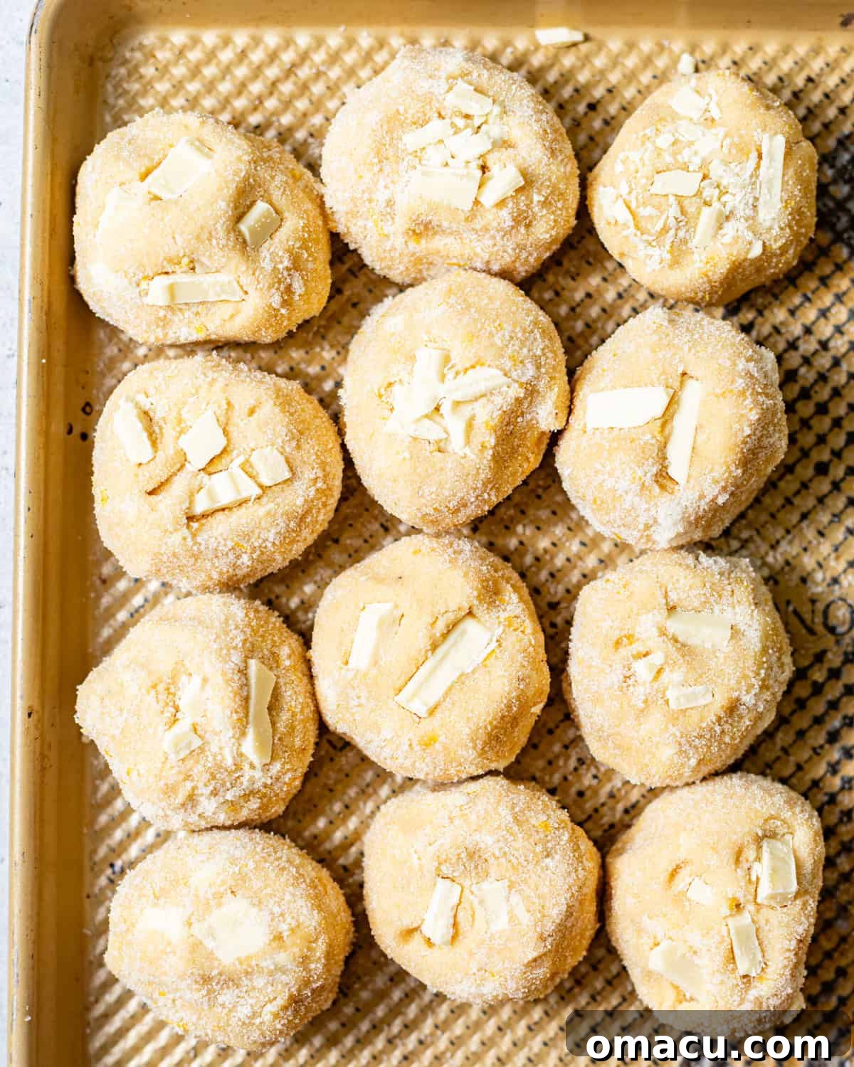 Zesty Lemon White Chocolate Chip Cookie Recipe 6 cookie dough balls on a baking sheet with white chocolate chunks pressed into the tops of the cookies.