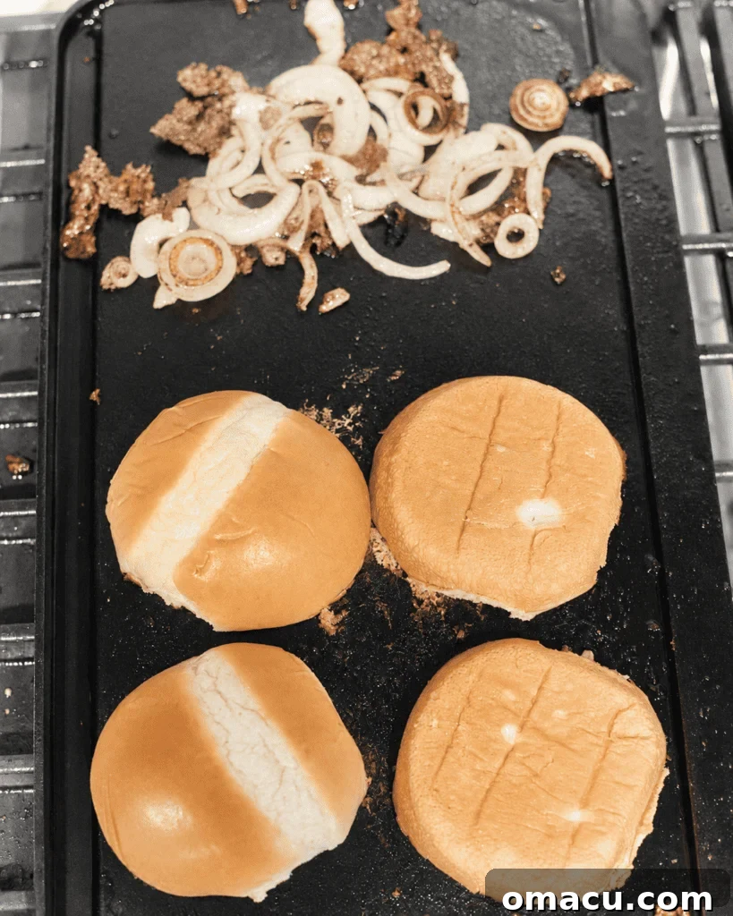 toasted hamburger buns on a griddle with fried onions on the side.