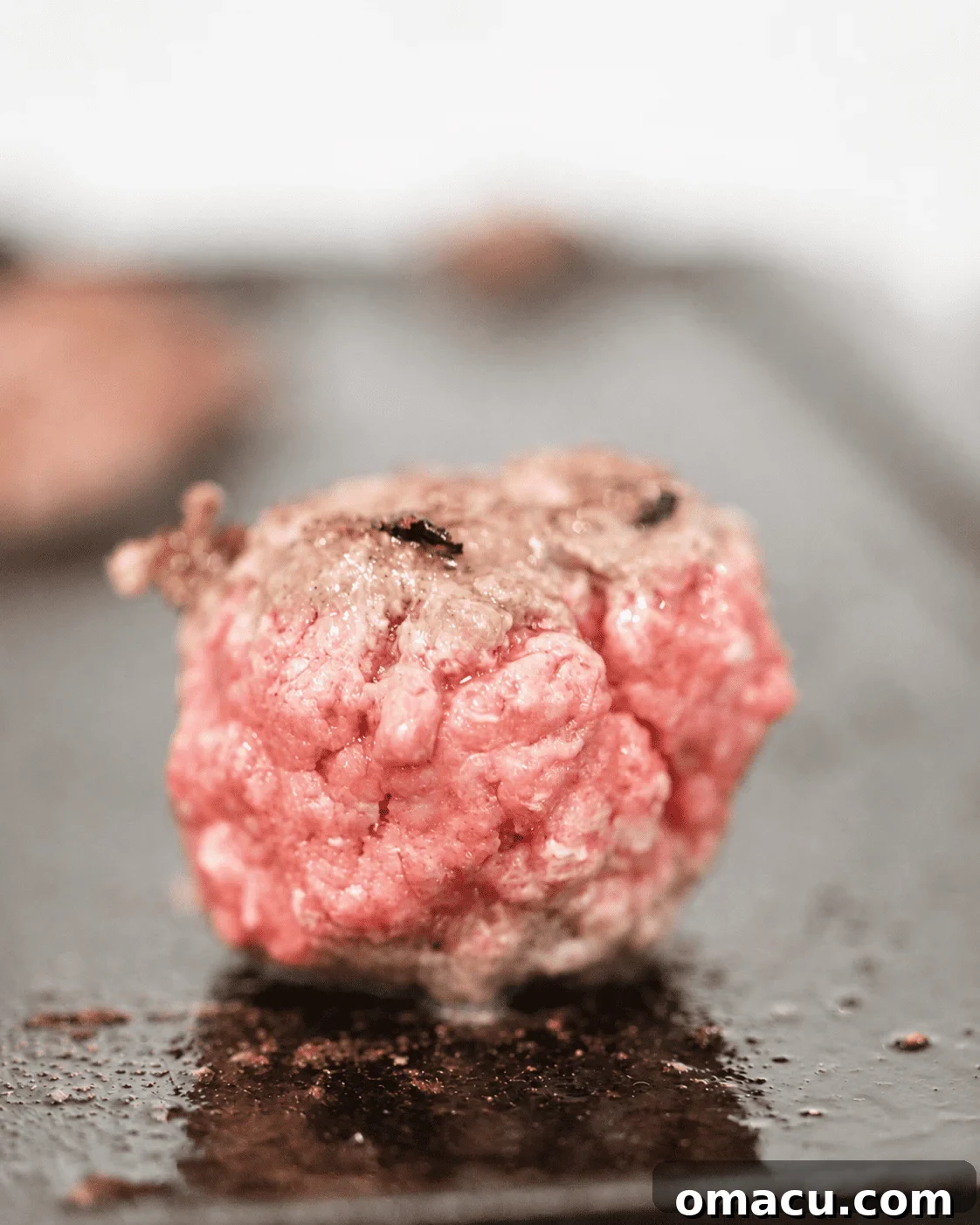 a ball of ground beef on a hot griddle before smashing with a burger press.