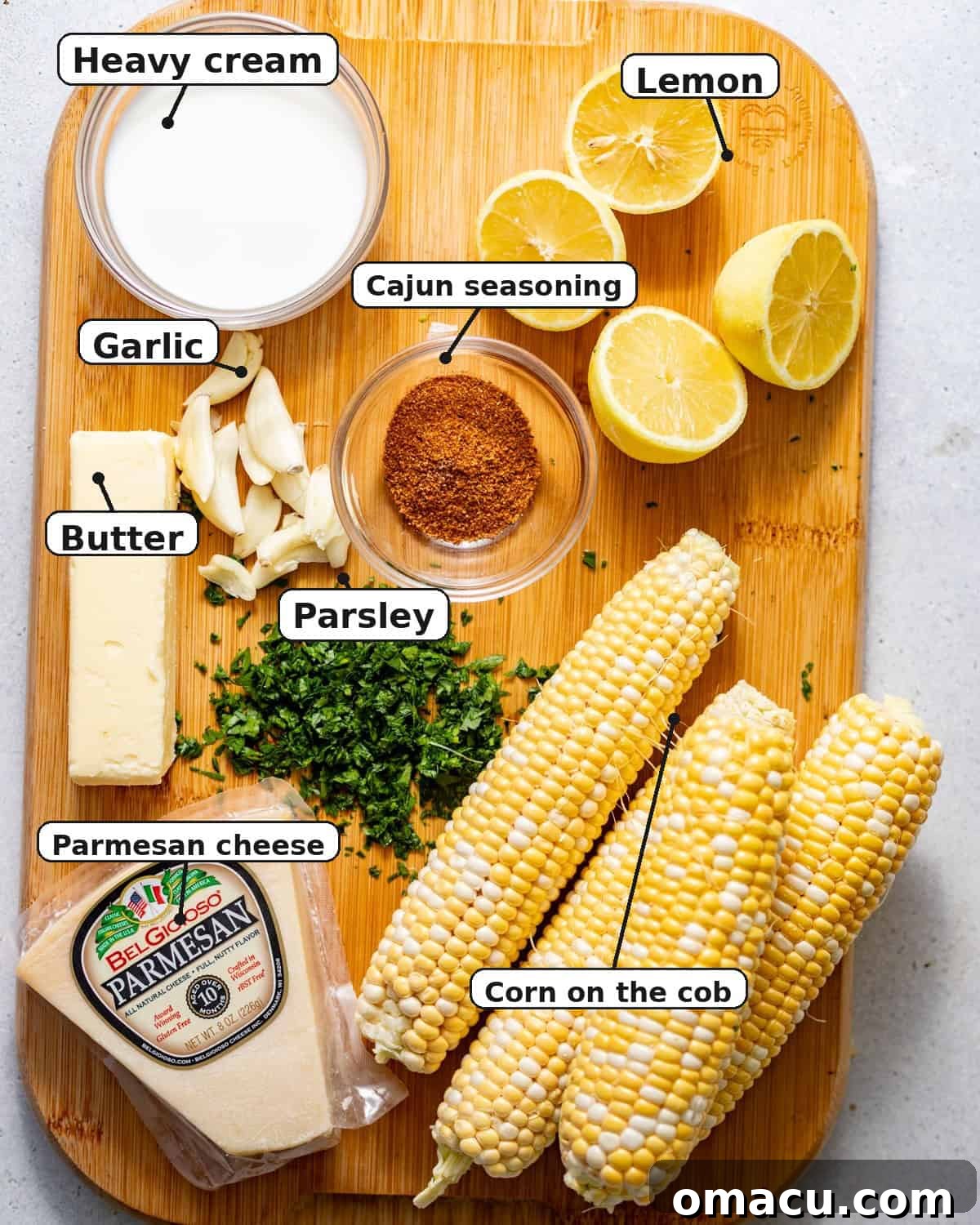 Oven-Baked Corn on the Cob with Garlic Herb Butter 3 ingredients to make baked corn on the cob on a cutting board - fresh corn on the cob, seasonings, garlic, parsley, butter, heavy cream, lemons, and parmesan.