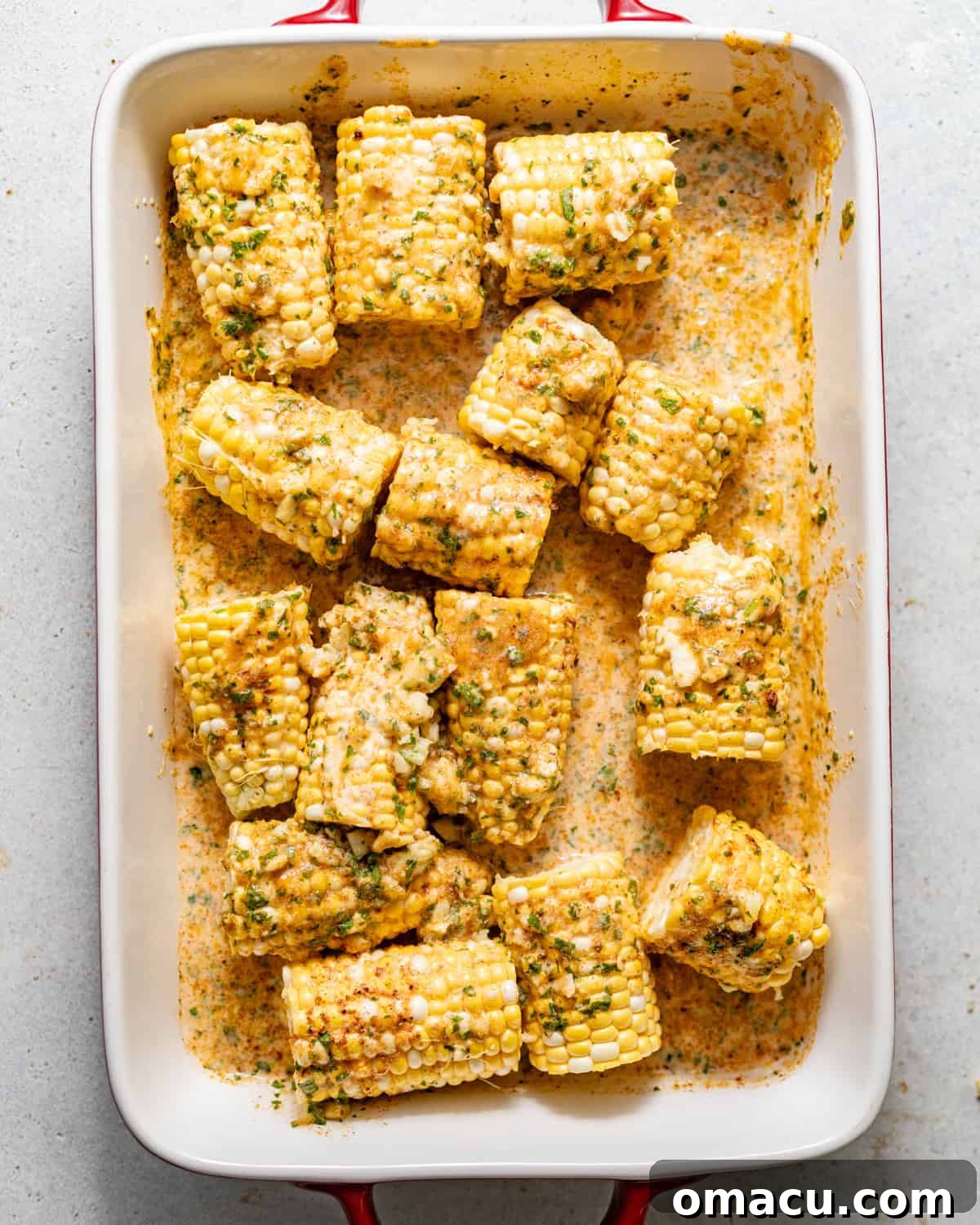 Oven-Baked Corn on the Cob with Garlic Herb Butter 5 corn on the cob in a baking dish covered in garlic butter.