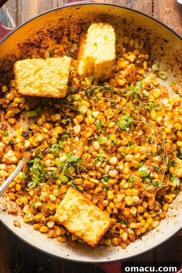 Oven-Baked Corn on the Cob with Garlic Herb Butter 7 blackened corn in a skillet with cornbread and fresh herbs on top for garnish.
