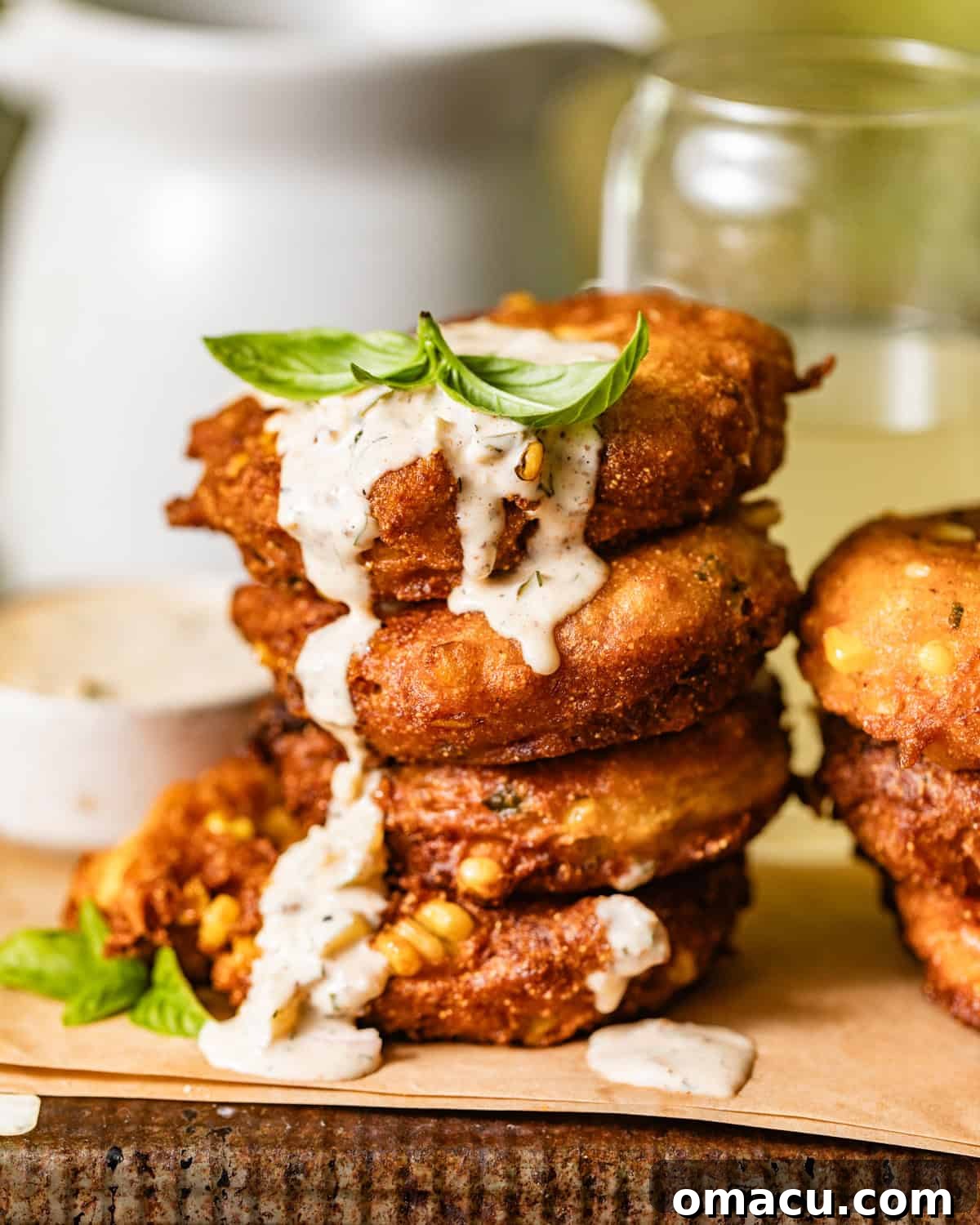 crispy corn fritters stacked on top of each other with dipping sauce drizzled down the sides.