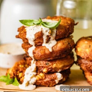 crispy corn fritters stacked on top of each other with dipping sauce drizzled down the sides.