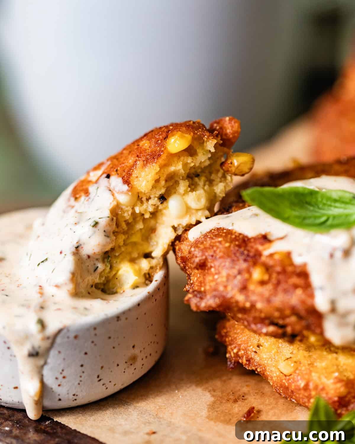 a corn fritter cut in half and dipped into a bowl of cajun remoulade.