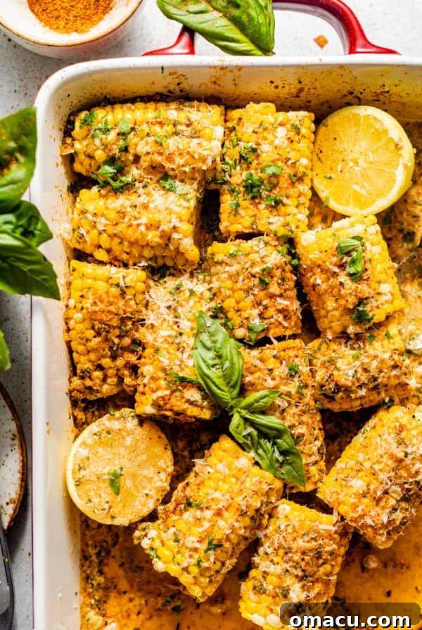 baked corn on the cob in a baking dish covered in garlic butter and fresh herbs.