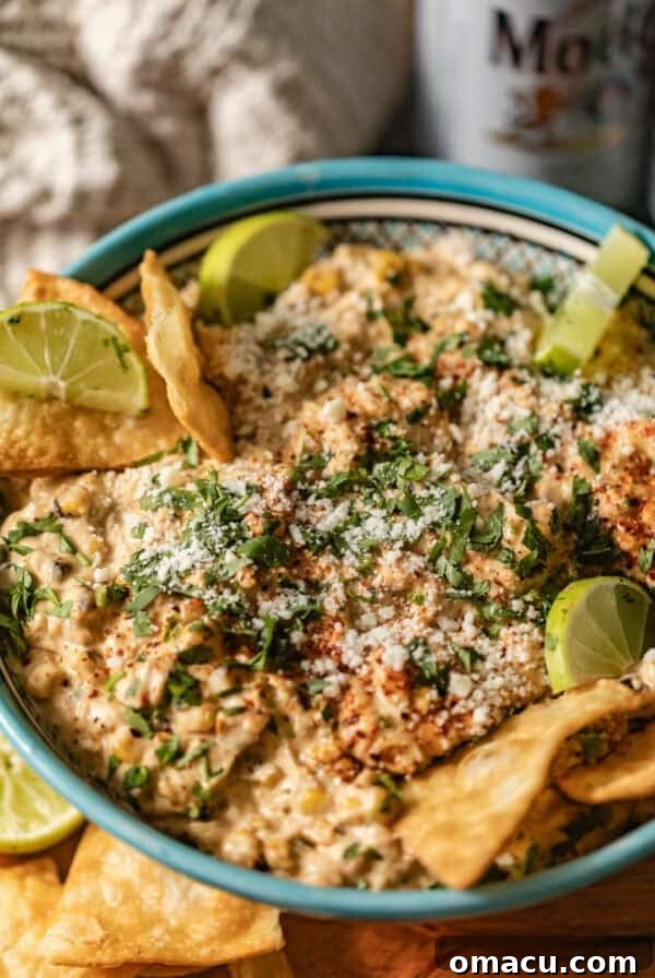 street corn dip in a bowl with limes and tortilla chips.