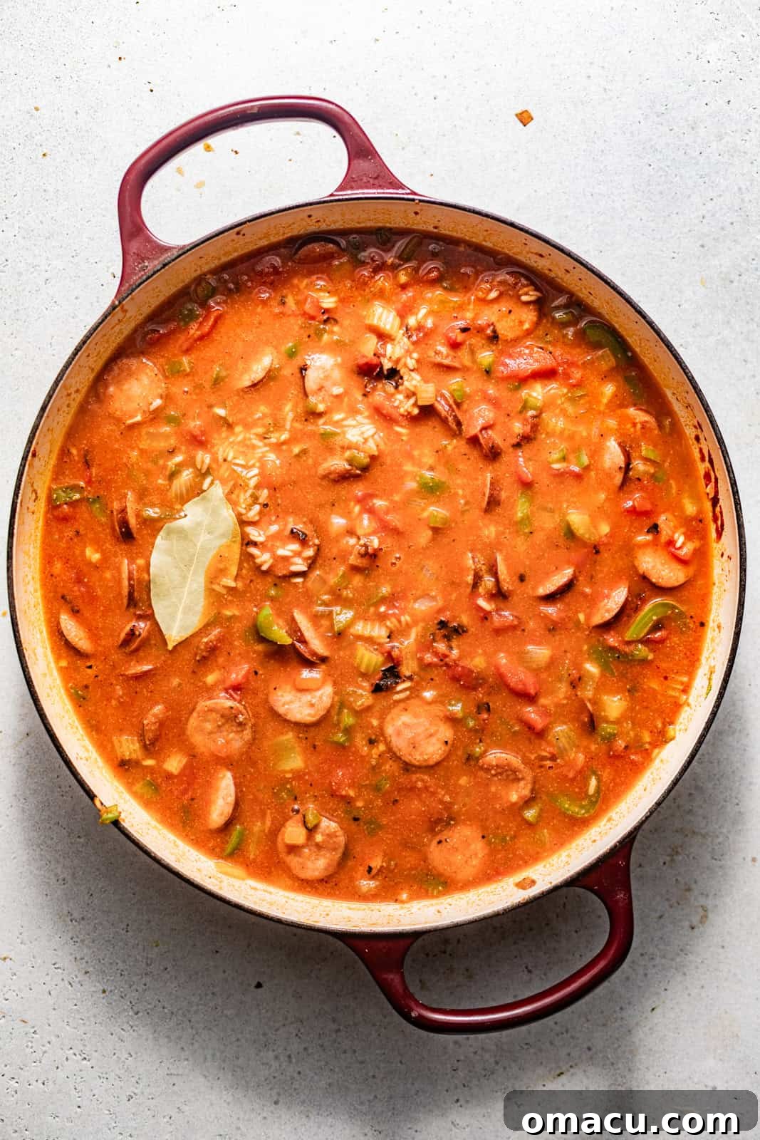 sausage, veggies, rice, and broth added to the skillet along with a bay leaf on top to simmer until the rice is fully cooked.