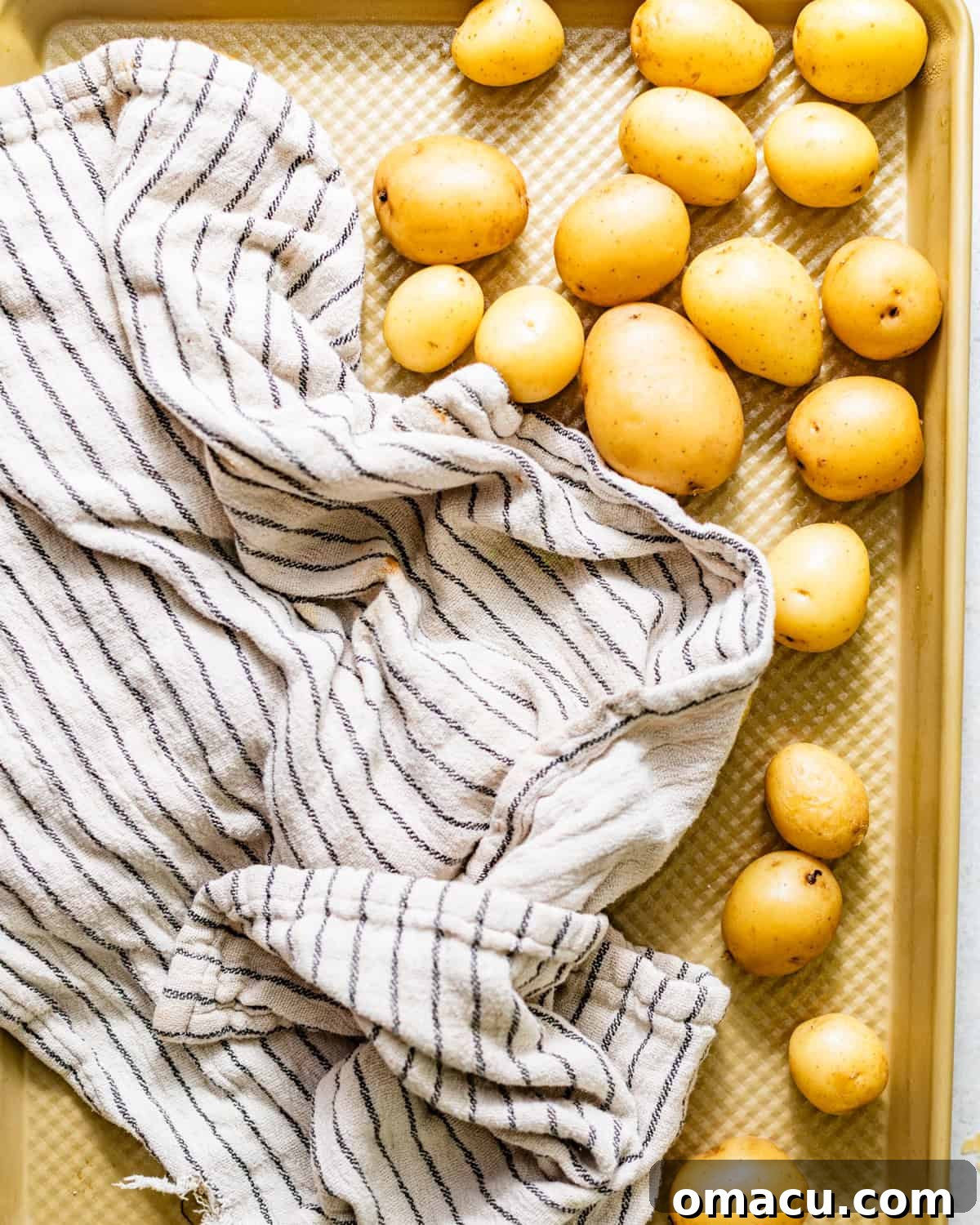 Crispy Garlic Parmesan Smashed Potatoes 5 cooked baby potatoes on a baking sheet being dried with a kitchen towel.