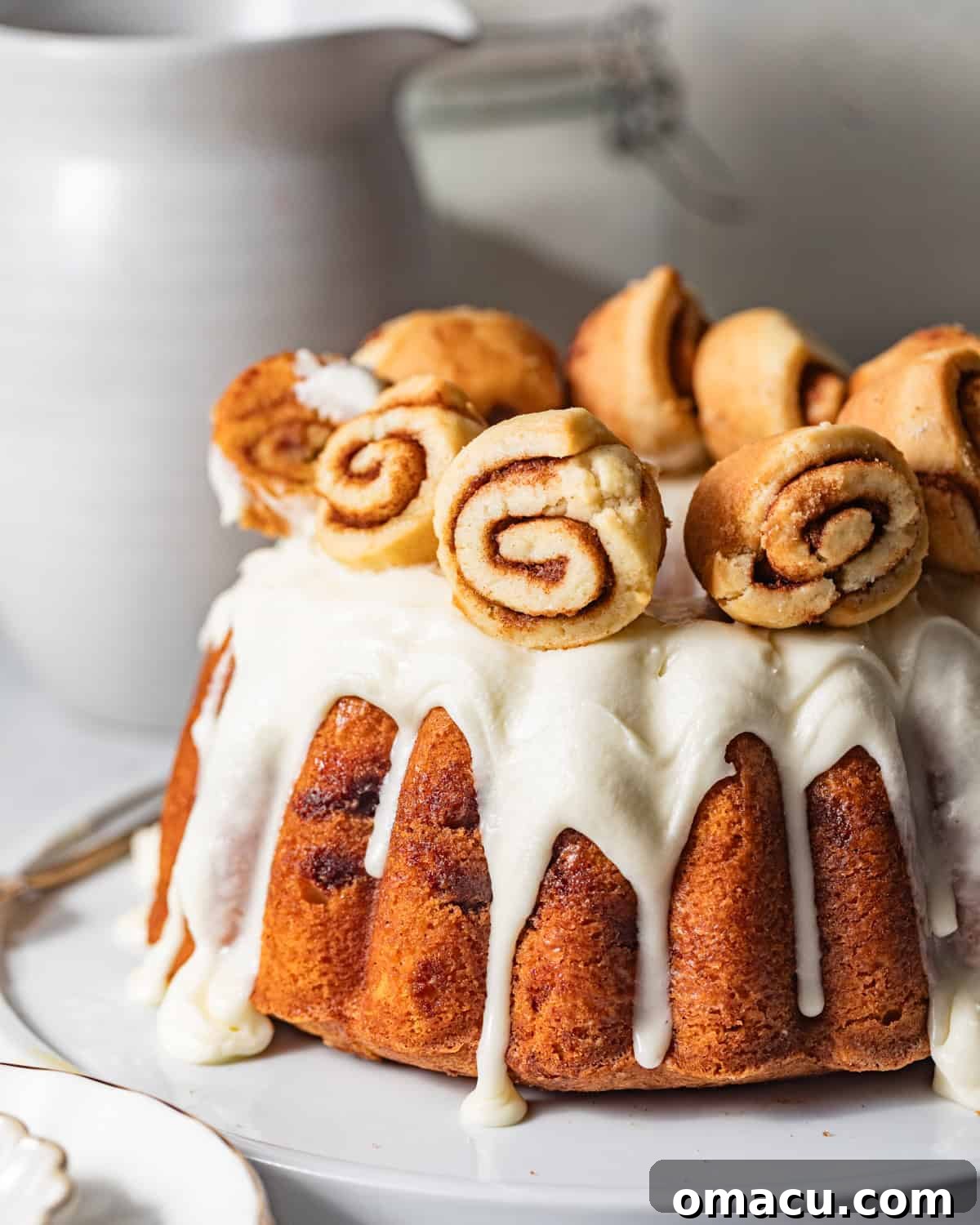 Sticky Cinnamon Roll Bundt Cake with Brown Sugar Glaze 2 cinnamon roll bundt cake on a cake plate topped with cream cheese glaze and mini cinnamon rolls for garnish.