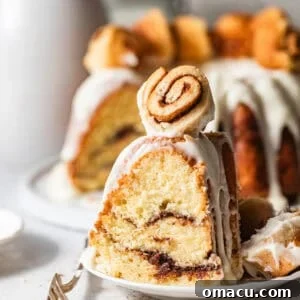 Sticky Cinnamon Roll Bundt Cake with Brown Sugar Glaze 13 a slice of cinnamon roll pound cake on a cake plate topped with a mini cinnamon roll.