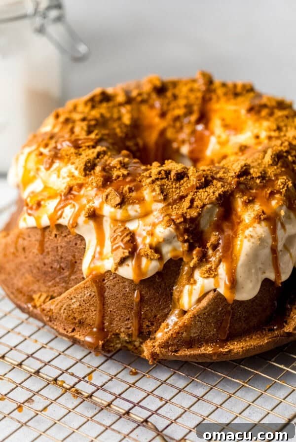 Sticky Cinnamon Roll Bundt Cake with Brown Sugar Glaze 9 cookie butter cake on a wire rack topped with salted caramel, biscoff cream cheese glaze, and crushed biscoff cookies.