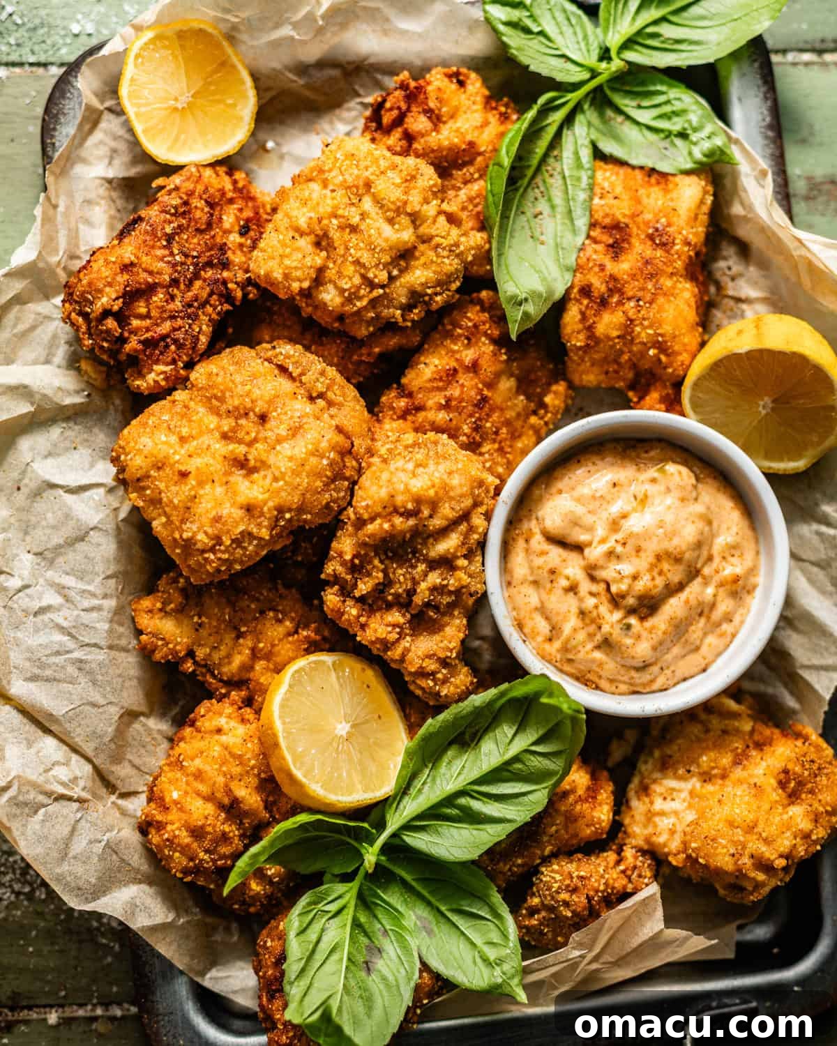 crispy catfish nuggets on a serving tray with Cajun tartar sauce with lemon wedges and fresh herbs on top for garnish.