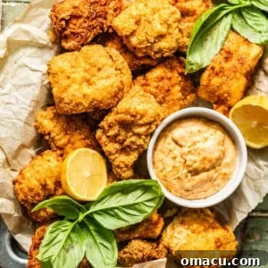 crispy catfish nuggets on a serving tray with Cajun tartar sauce with lemon wedges and fresh herbs on top for garnish.