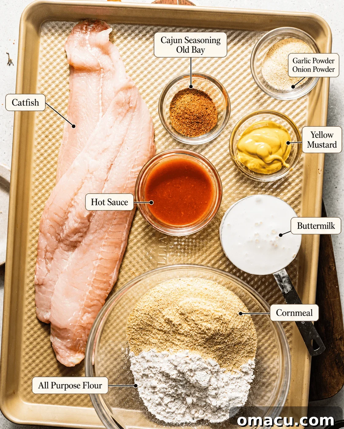 ingredients to make catfish nuggets on a baking sheet - catfish fillets, cornmeal, flour, buttermilk, yellow mustard, hot sauce, and seasonings.