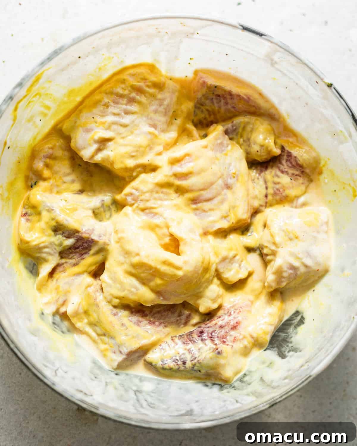 catfish nuggets in a bowl covered in seasonings and yellow mustard.